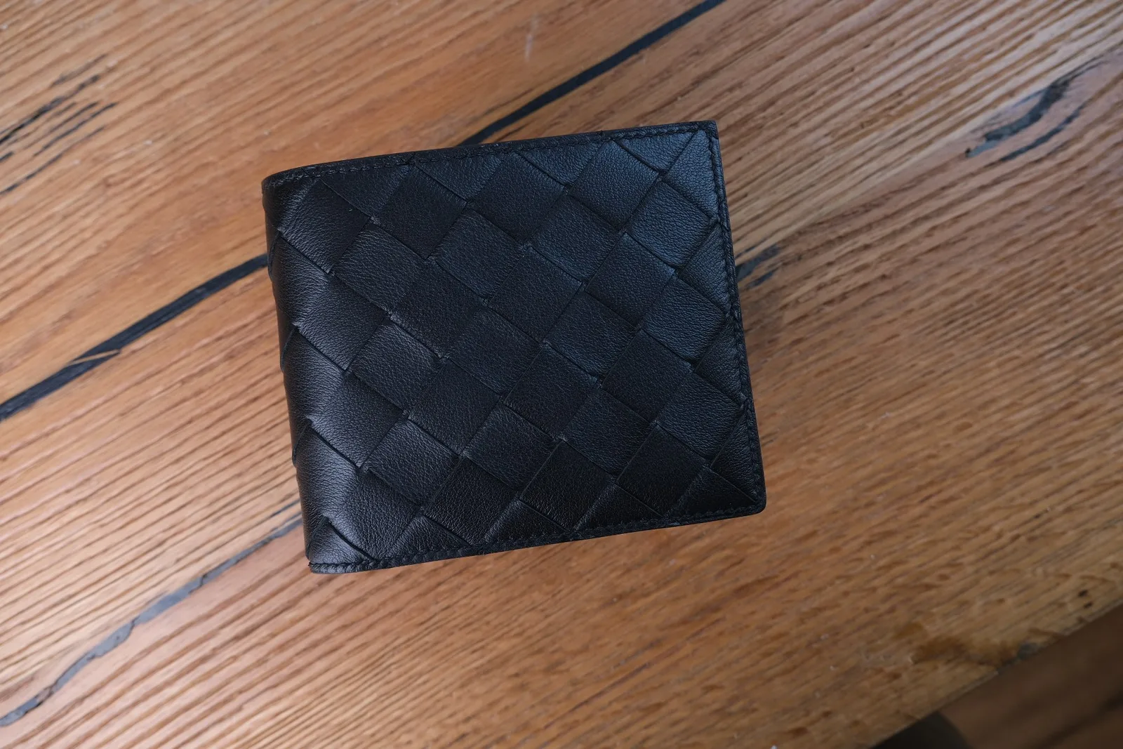 Ví gập đôi Bottega Veneta màu đen đặt trên mặt bàn gỗ sau khi xử lý spa