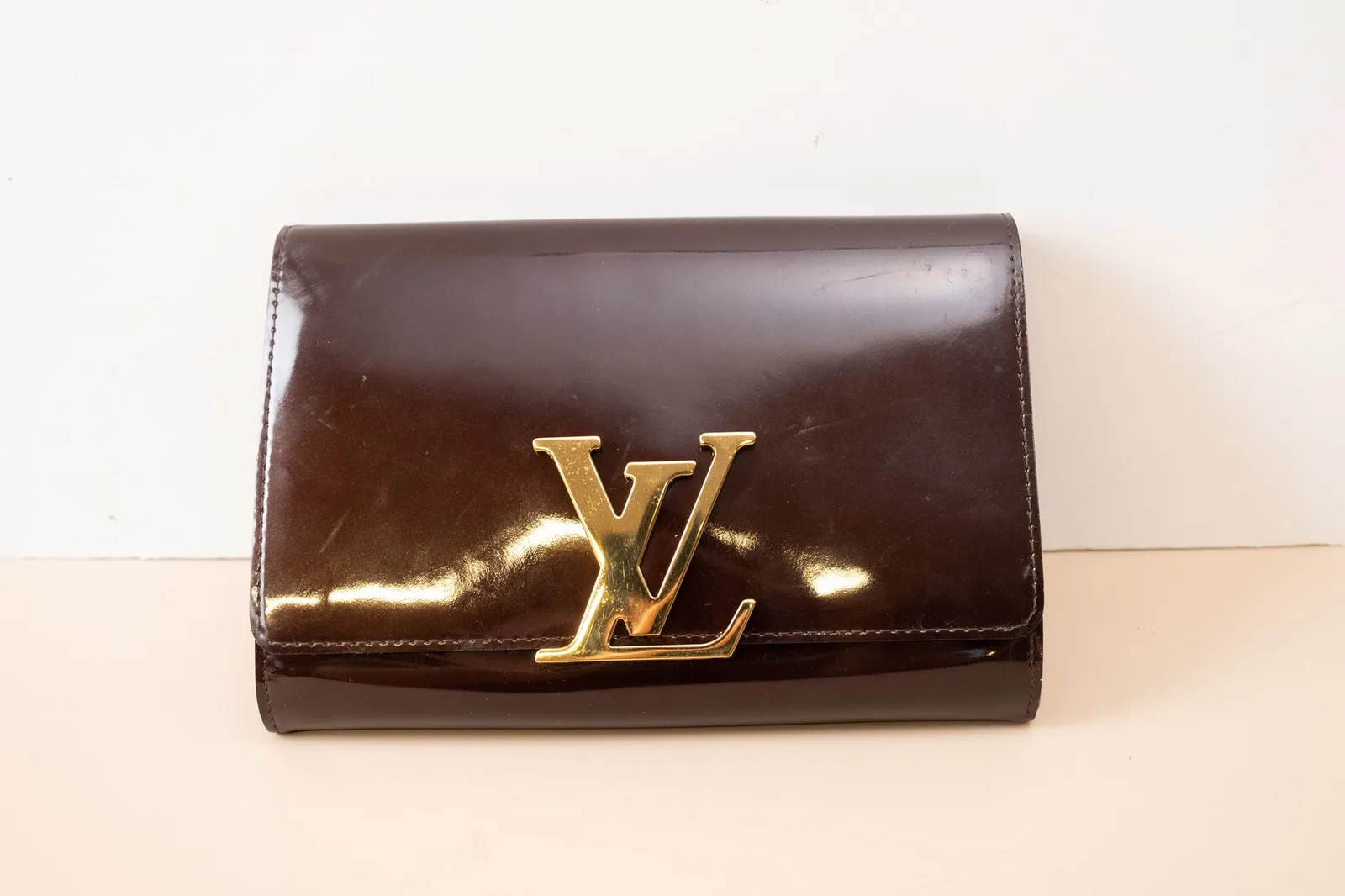 Mặt trước clutch Louis Vuitton Louise da bóng màu nâu với logo kim loại LV màu vàng