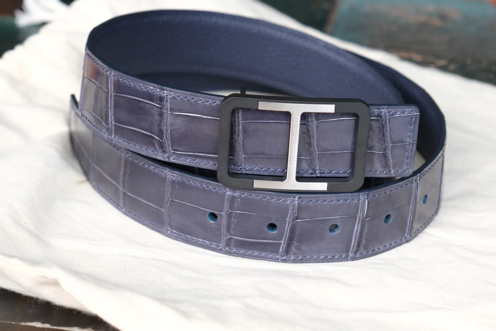 Thắt lưng cá sấu Hermès đặt trên khăn vải thấy rõ phần lỗ cài và mặt khoá chữ H